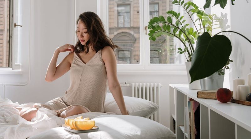 Asian woman in a cozy bedroom enjoying a calm morning with fresh citrus slices on a bed.